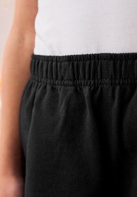 Pantalons en coton noirs avec une taille élastique, présentant une texture douce et un design froncé le long de la taille. Le tissu semble léger.