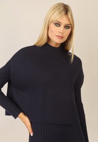 Marineblauer, kurzer Pullover mit gerippten langen Ärmeln und hohem Halsausschnitt, der eine weiche Textur und eine lockere Passform bietet.