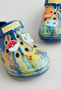 Sabots à motif bleu et orange avec des embellissements de personnages Pokémon : Pikachu, Bulbizarre, Salamèche et une Poké Ball.