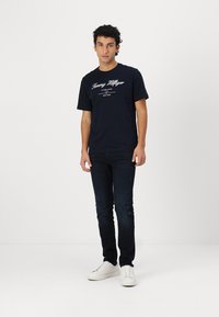 Granatowa bawełniana koszulka z białym napisem "Tommy Hilfiger", w komplecie z ciemnoniebieskimi dżinsami i białymi sneakersami.