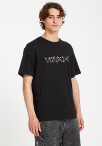 Black cotton t-shirt with short sleeves and a round neckline, featuring a white logo graphic on the front. It has a relaxed fit.