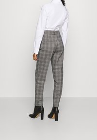 Gray plaid trousers with a high waist and tapered legs, made of a smooth fabric. Paired with black high-heeled ankle boots.