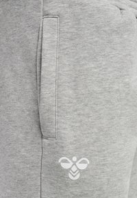 Grijze sweatpants met een klein wit bijenlogo op het lagere gedeelte van de zak, gemaakt van zacht, textuurachtig katoen met zijzakken.