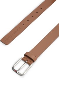 Καφέ δερμάτινη ζώνη με ασημένια μεταλλική αγκράφα, με ορθογώνιο σχήμα και αρκετές τρύπες για ρυθμίσεις. Το όνομα της μάρκας είναι ανάγλυφο στο λουρί.