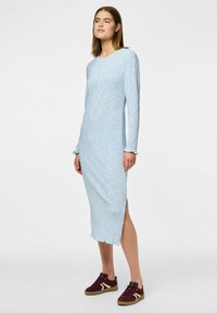 Vestido azul de manga larga con un patrón floral, textura acanalada, aberturas laterales y dobladillo con volantes, combinado con zapatillas bajas burdeos.