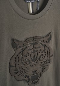 Maslinasto zeleni pamučni majica s reljefnim dizajnom tamnosive tigra na prednjem dijelu, klasičnog kroja i redovite fit.