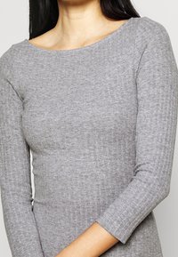 Top long à manches longues gris à côtes avec un décolleté large, présentant une texture douce et une silhouette ajustée. Les manches sont légèrement ajustées au poignet.