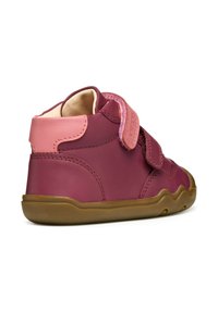 Zapato de cuero burdeos de caña alta con acentos en rosa, correa de Velcro y suela de goma con un borde ondulado. Textura suave, diseño redondeado.