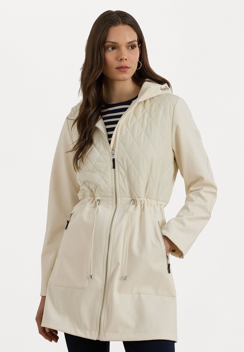 Light beige jacket with a quilted upper section and solid lower part. Features a zip closure, adjustable drawstring waist, and side pockets.
