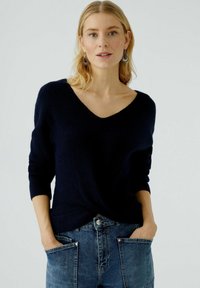 Pull en maille bleu marine avec un col en V et des manches trois-quarts. Assorti à un jean taille haute avec de grandes poches avant.