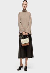 Suéter de punto beige de cuello alto, falda midi de cuero negra y zuecos negros. Bolso pequeño de patrón en crema y marrón con cadena.