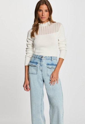 Pull blanc avec un col texturé et ondulé, et un panneau rayé transparent ; associé à un jean en denim bleu clair taille haute avec poches.