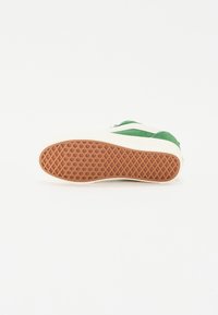 Grønn og hvit sneakers med en teksturert gummisåle, som har et geometrisk mønster og en glatt overdel med to grønne striper.