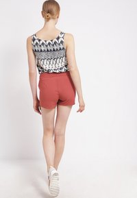 Pantaloni corti rossi con vita aderente e una canotta a righe bianche e nere. L'outfit presenta una silhouette ampia e una texture di tessuto morbida.