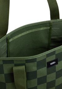 Zielona torba w kratę wykonana z trwałej tkaniny, z dwoma górnymi uchwytami i wewnętrzną kieszenią. Na zewnątrz znajduje się czarna naszywka z logo Vans.