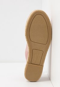 Semelle d'une espadrille taille 37 avec une semelle extérieure en caoutchouc marron texturé et une semelle intermédiaire enveloppée de jute, appuyée contre un mur d'angle blanc.