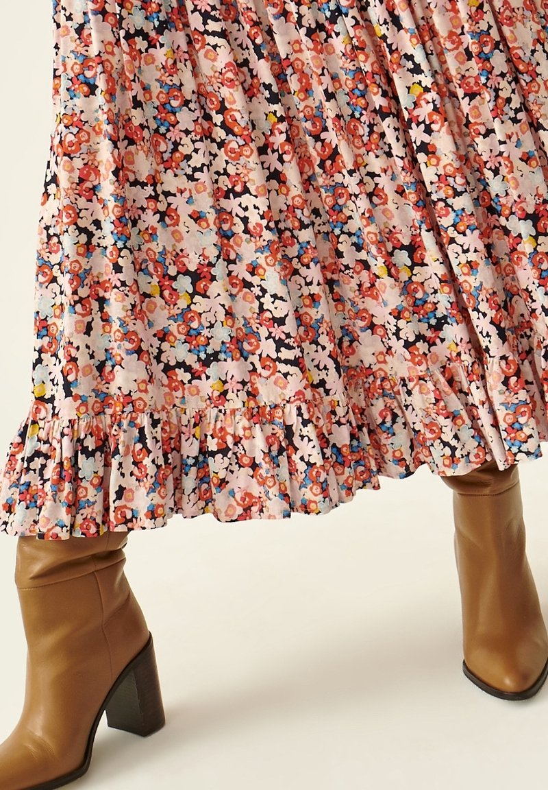 Jupe midi à motif floral avec ourlet à volants, associée à des bottines en cuir camel à talons hauts sur fond clair.