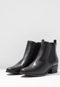 Botas de tobillo de piel negra con un acabado suave, paneles elásticos y un tacón bajo apilado, con punteras redondeadas y costuras mínimas.