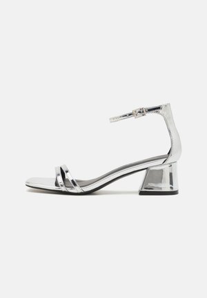 Zilveren sandalen met hak en een spiegelende afwerking. Voorzien van twee dunne bandjes over de voorkant en een enkelbandje met een gesp. Design met blokhak.
