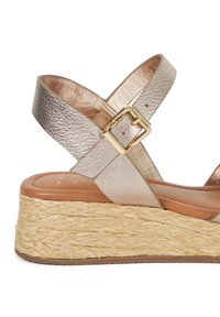 Metallic leather wedge sandal with adjustable ankle strap, featuring a woven jute platform sole and a smooth, padded footbed in neutral tones.