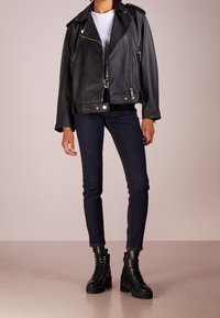 Chaqueta de moto de cuero negra con herrajes plateados, bolsillos con cremallera y un corte relajado, combinada con pantalones de mezclilla oscuros y botas negras con cordones.