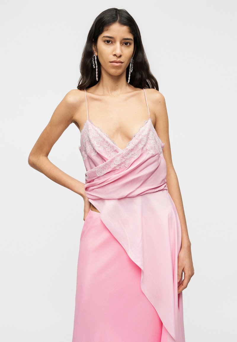 Robe en satin rose avec bordure en dentelle, présentant un décolleté en V plongeant, des bretelles fines et un design drapé asymétrique. Texture lisse et tissu fluide.