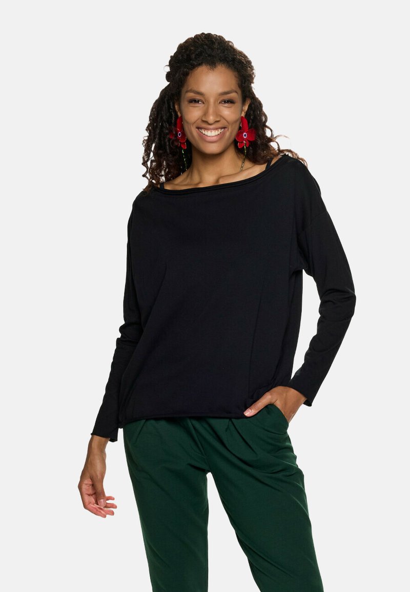 Czarna bluzka z długim rękawem o szerokim dekolcie i luźnym kroju, zestawiona z zielonymi spodniami. Materiał wydaje się być miękki, o gładkiej fakturze i ładnym opadzie.