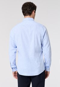 Camicia azzurra a manica lunga con un tessuto testurizzato, colletto a punta, polsini con bottoni e orlo curvo, caratterizzata da sottili variazioni di colore.