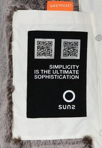 Tessuto bianco con un'etichetta nera che presenta due codici QR. Il testo recita "La semplicità è la massima sofisticazione" e il nome del marchio "suns". La linguetta arancione riporta la scritta "Safe Pocket".