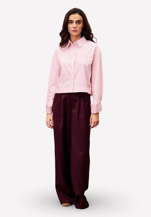 Korte roze gestreepte crop top met een kraag, gecombineerd met wijde, donker bordeauxrode broeken. Opvallende knoopdetails op het shirt en plooien op de broek.