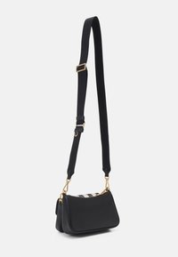 Sac à main noir avec une texture lisse, des accessoires en or et une bandoulière ajustable. Présente une fermeture zippée en haut et un accent supérieur à motifs.