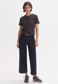 T-shirt bleu marine texturé avec un motif de vagues, associé à un jean large bleu foncé. Une ceinture marron accentue la taille, le tout complété par des baskets grises.