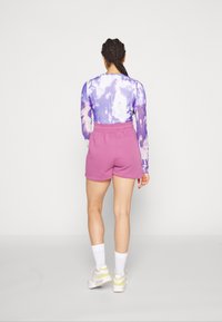 Långärmad lila tie-dye tröja med ribbad textur, parat med rosa bomullsshorts. Vita sportstrumpor och skor fullända outfiten.