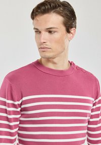 Pull en stripe rose avec des rayures horizontales blanches, texture côtelée, col rond et trois boutons en accent sur l'épaule gauche.