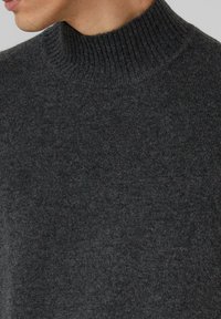 Uomo che indossa un maglione a collo alto a coste di un grigio scuro, che mostra il colletto e l'area superiore del petto.