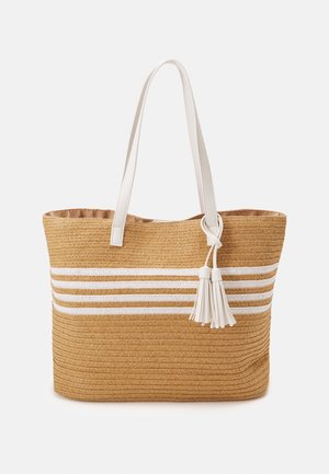 Sac en paille couleur tan avec des rayures horizontales blanches. Doté de longues poignées blanches et d'un pompon décoratif blanc. Doublure intérieure lisse.