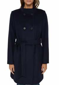 Marineblauw dubbel-breasted jasje met hoge kraag, zwarte knopen, zijzakken en een bijpassende riem, gemaakt van een zachte, gestructureerde stof.