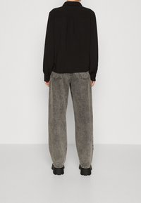 Black long-sleeve shirt with a back pleat, paired with loose-fit gray denim jeans featuring contrast stitching and a relaxed silhouette.