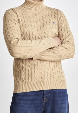 Beige Rollkragenpullover aus Kabelstrick mit gerippten Bündchen und Saum. Verfügt über ein strukturiertes Muster und ein kleines Logodetail auf der Brust.