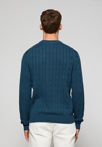 Donkerblauwe kabelgebreide trui, met lange mouwen, ronde halslijn en geribde zoom. Het textuurpatroon verhoogt de visuele interesse.