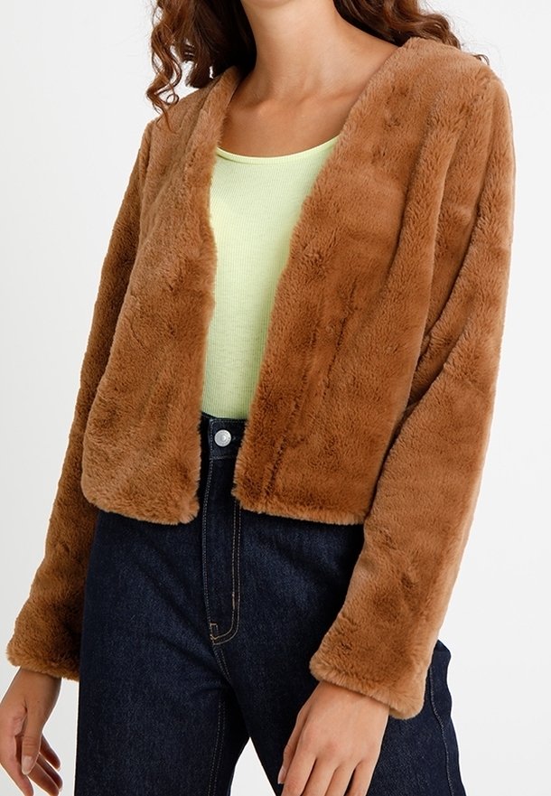 Giacca corta in pelliccia sintetica marrone con scollatura a V, maniche lunghe e texture morbida, abbinata a un top verde chiaro e jeans in denim scuri.