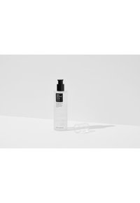 Bouteille en plastique transparent avec un bouchon-pompe noir, étiquetée "Liquide décoloré BHA." Forme cylindrique, texture lisse, avec un capuchon transparent assorti à proximité.