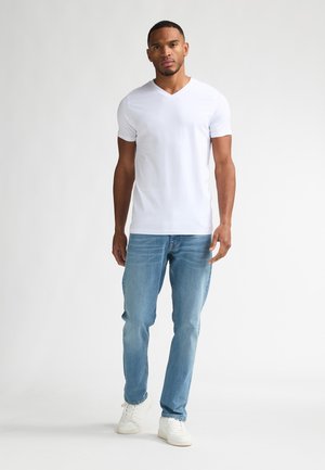 Weißes V-Ausschnitt-T-Shirt mit kurzen Ärmeln, kombiniert mit hellblauen Denim-Jeans und weißen Turnschuhen. Glatte Textur, klassischer lässiger Look.