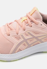 Bottine de sport rose clair avec dessus en maille, superpositions synthétiques, semelle blanche épaisse et accents jaunes contrastants sur la languette et le logo.