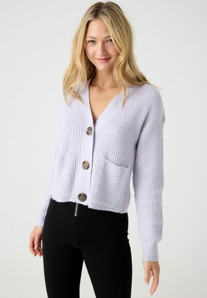 Cárdigan de punto lavanda con escote en V, que presenta cuatro botones grandes, dos bolsillos frontales y textura acanalada. Combinado con pantalones negros.
