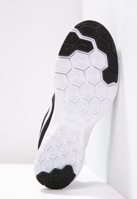 Podešev černo-bílé běžecké boty Nike s hexagonálním vzorkem pro trakci, opřená o bílou zeď.