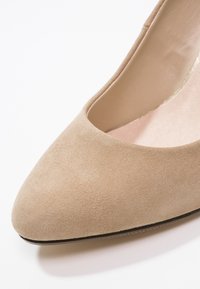 Chaussure plate pour femme en daim beige, bout fermé arrondi, semelle intérieure lisse et semelle fine sur fond blanc.
