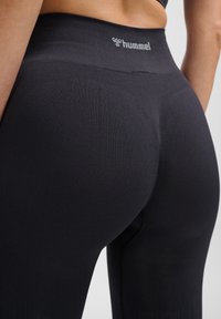 Svarta högmidjade leggings tillverkade av elastiskt material, med en logotyp vid midjan och en slät, sömlös design med en figursydd siluett.