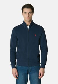Giacca zip-up blu navy realizzata in tessuto misto cotone, con colletto rialzato, polsini a coste e un piccolo logo rosso sul lato sinistro del petto.