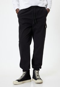 Sorte cargo-bukser med elastisk talje, sidelommer og opsmøgede afslutninger. Båret med højtstående sorte sneakers og en hvid sweatshirt.